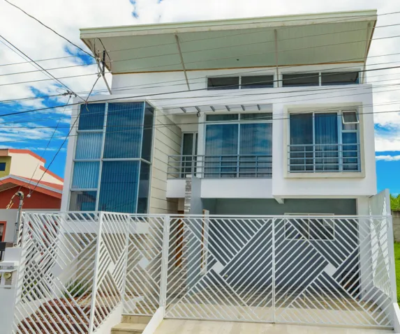 Contemporary multi-level exterior featuring a slanted roofline, floor-to-ceiling glass paneling, metal balcony railings, and a geometric-patterned metal privacy gate