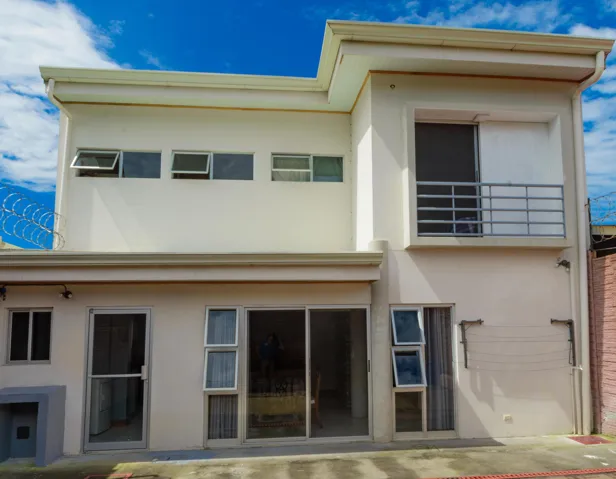 Two-story exterior featuring a smooth stucco finish, metal balcony railing, large sliding glass door, and operable horizontal awning windows