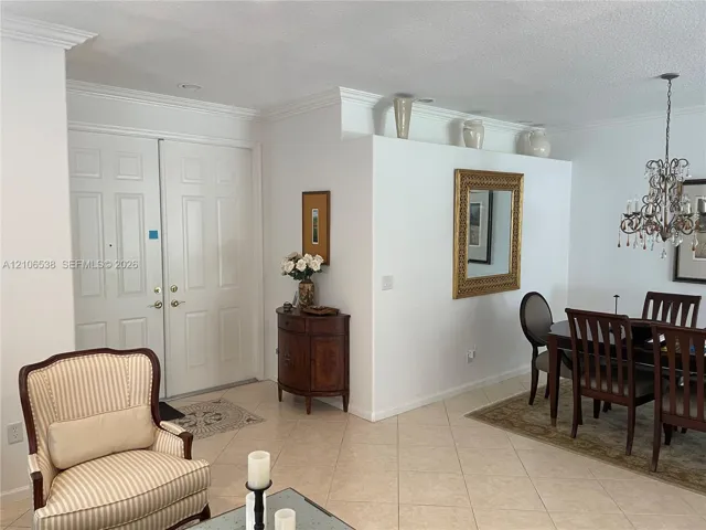 Double-door entry featuring crown molding, neutral tile flooring, and a decorative multi-arm crystal chandelier