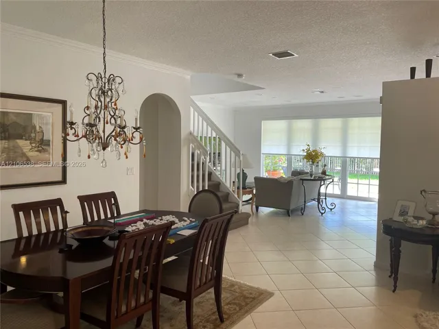 Open-concept interior featuring large-format ceramic tile flooring, an ornate wrought-iron chandelier, architectural arched entryway, and a staircase with a white wood balustrade