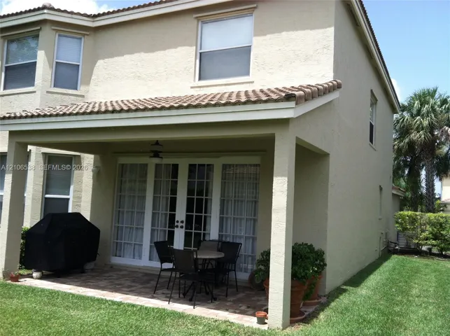 Stucco exterior featuring a covered patio with tile flooring and a ceiling-mounted light fixture, complemented by French door access and a tile roof
