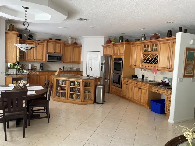 Kitchen featuring wood cabinetry, integrated wine storage, an island with glass-front display cabinets, double wall ovens, and stone-finish countertops