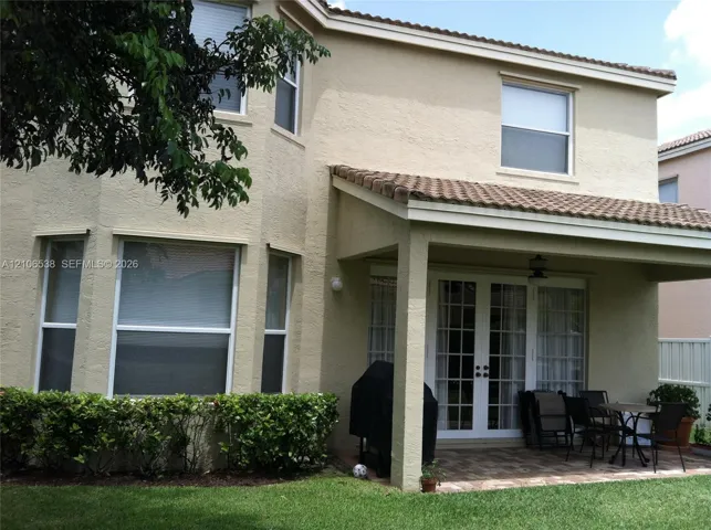 Stucco exterior featuring a covered patio with paved flooring and multi-pane French doors