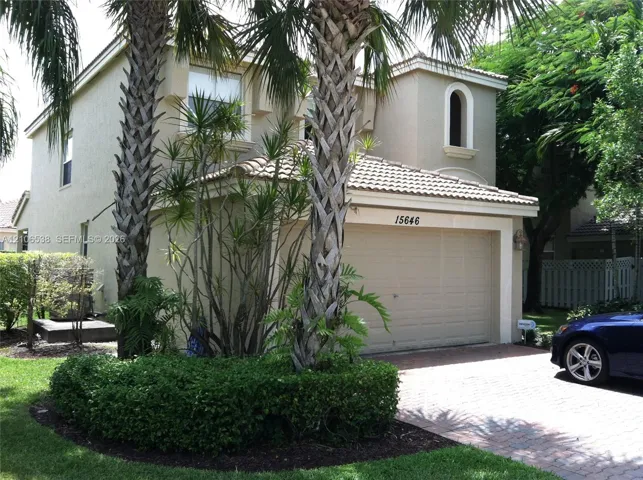 Two-story stucco exterior featuring a tile roof, an arched upper-level window, and a paver driveway leading to a multi-car garage
