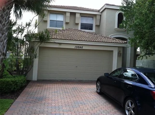 Stucco exterior featuring a two-car garage, tile roofing, an arched entryway, and a paved stone driveway