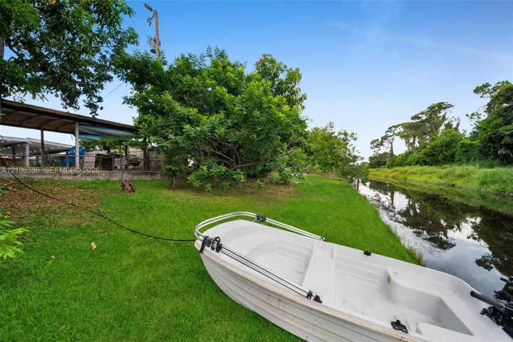Waterfront parcel featuring a lawn, mature trees, and a covered patio structure