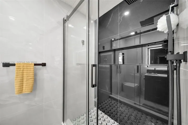 Walk-in shower featuring a glass enclosure with matte black hardware, large-format tile surround, rainfall showerhead, and a geometric patterned tile​​‌​​​​‌​​‌‌​‌‌​​​‌‌​‌​‌​‌​​​‌​​ floor