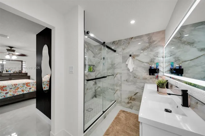 Walk-in shower with floor-to-ceiling large-format tile surround and frameless glass door, dual-sink vanity with matte black faucets, and integrated LED-backlit mirror