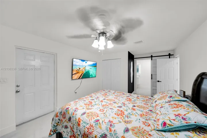 White paneled interior door, sliding white barn-style door with matte black hardware, and overhead ceiling fan with multi-light fixture