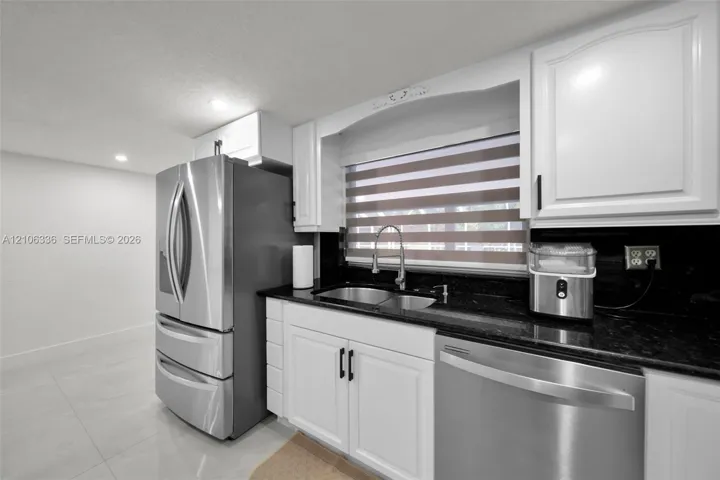 Kitchen featuring white cabinetry, dark stone countertops, stainless steel refrigerator and dishwasher, double-basin undermount sink, and recessed lighting
