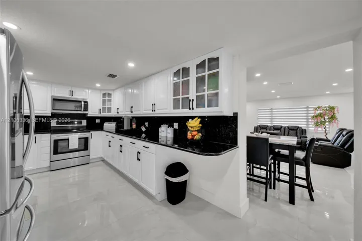 Kitchen featuring white shaker-style cabinetry, black stone countertops, stainless steel appliances, glass-front upper cabinet doors, and polished large-format tile flooring