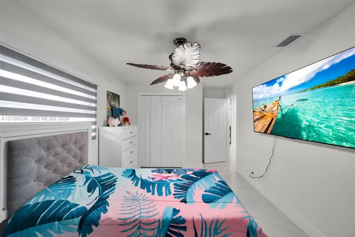 Room featuring neutral wall tones, large-format tile flooring, a multi-blade ceiling fan with integrated lighting, and dual-pane windows with banded roller shades