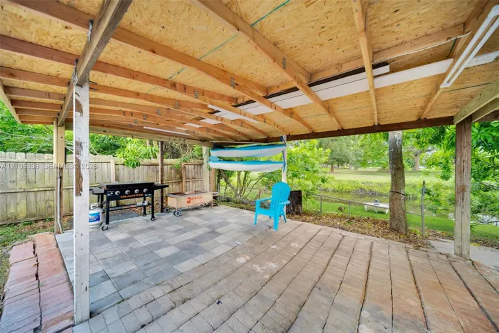 Covered outdoor living space featuring a wood-beam structure, stone paver flooring, and a fenced perimeter