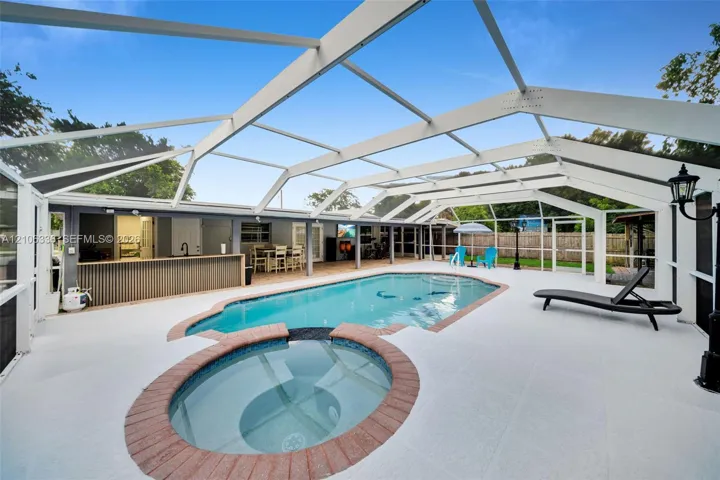 Screened-in pool area featuring a built-in spa with masonry surround, a covered wet bar, and light-toned hardscaping