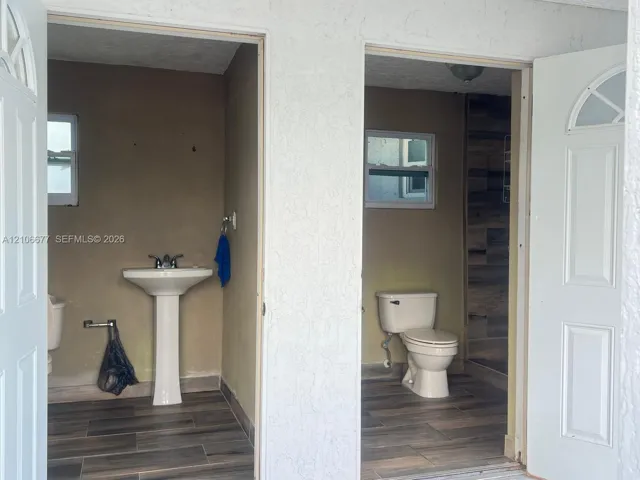 Dual entryways featuring white paneled doors, wood-finish flooring, a white pedestal sink, and a walk-in shower with wood-patterned tile surrounds