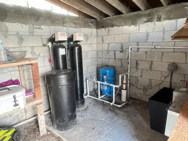 Utility area featuring concrete masonry unit walls, a dual-tank water treatment system, and a blue pressure tank