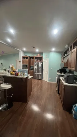 Kitchen featuring wood-finish cabinetry, stone-style countertops, stainless steel appliances, and wood-finish flooring