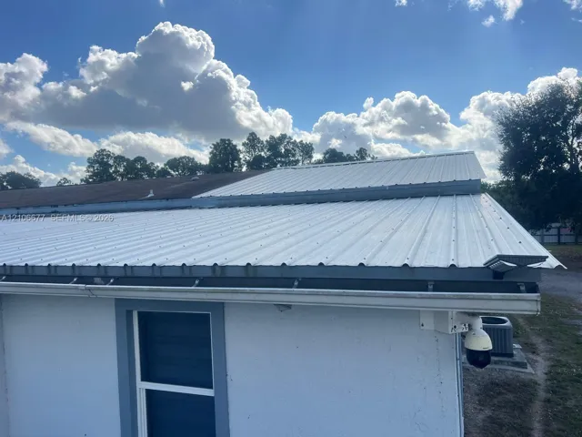 Standing seam metal roofing, white exterior finish, integrated gutter system, and security camera fixture