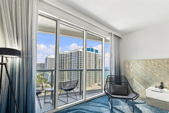 Floor-to-ceiling windows, private balcony with metal railing, and decorative wood-panel accent wall