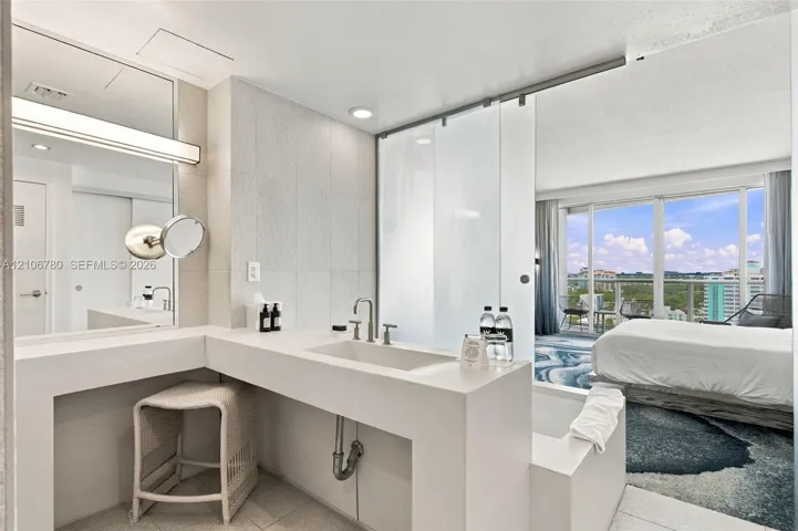 Custom vanity with a solid-surface countertop and integrated sink, brushed metal fixtures, large wall-mounted mirror with integrated lighting, and a floor-to-ceiling glass panel partition