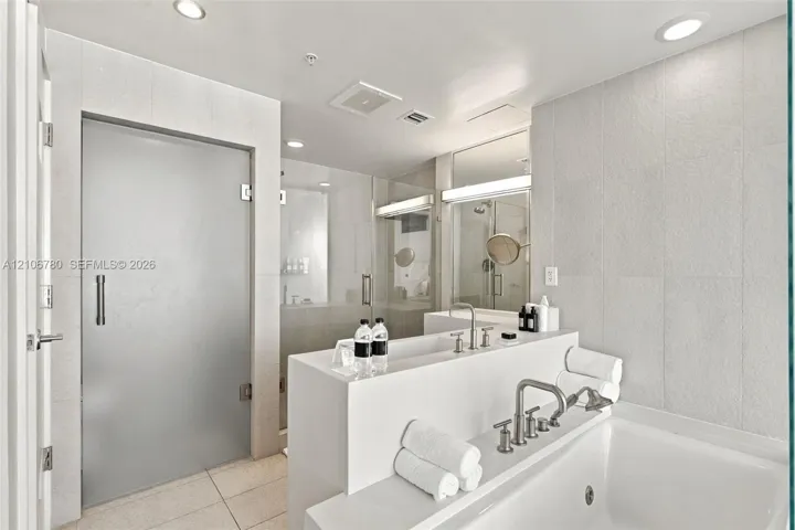 Bathroom featuring a deep soaking tub, polished nickel deck-mounted faucet, custom solid-surface vanity, walk-in glass-enclosed shower, and floor-to-ceiling tile surrounds
