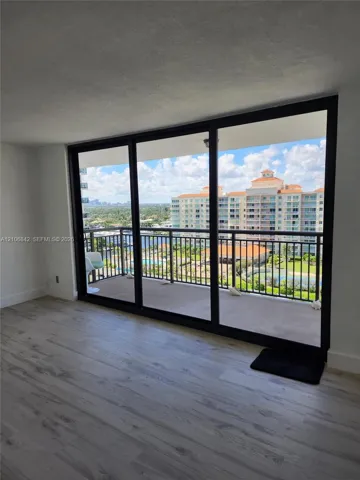 Floor-to-ceiling glass sliding doors opening to a covered balcony with metal railings and light-toned wood-finish flooring