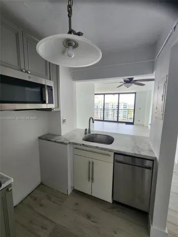 Kitchen area featuring light-toned cabinetry, stainless steel appliances, stone-finish countertops, an undermount sink with a gooseneck faucet, and wood-finish flooring