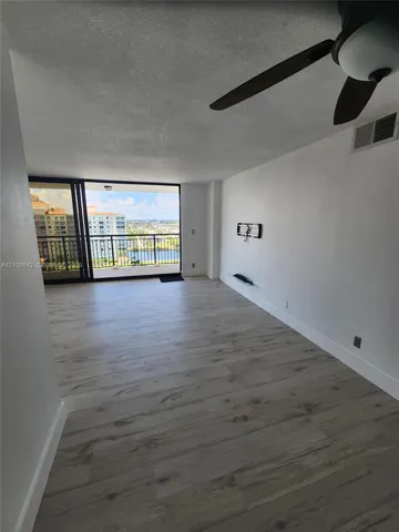 Interior space featuring wood-finish flooring, ceiling fan, and sliding glass doors leading to a balcony with water and building scenery