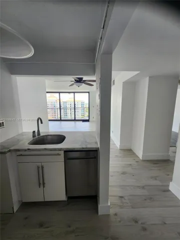 Kitchenette featuring stone-finish countertops, stainless steel sink, under-counter stainless steel dishwasher, and wood-finish flooring