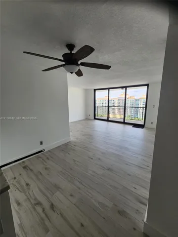 Open-concept interior featuring light wood-finish flooring, a ceiling fan with integrated lighting, and floor-to-ceiling sliding glass doors opening to a balcony with metal railing