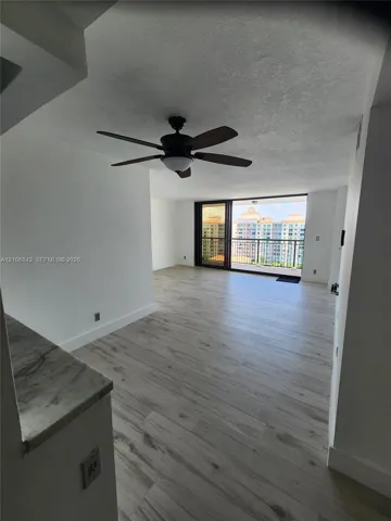 Light-toned wood-finish flooring, stone-surfaced counter, ceiling fan with integrated lighting, and full-height sliding glass doors leading to a balcony