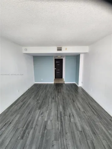 Interior room featuring wood-finish flooring, textured ceiling, and a dark-toned door with horizontal panel detailing