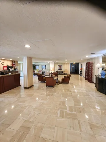 Expansive lobby featuring polished stone tile flooring, built-in reception desk with wood-veneer finish, recessed lighting, and vertical-stripe wall coverings