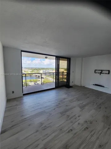 Open-concept living space featuring wood-finish flooring, floor-to-ceiling sliding glass doors, and a covered balcony with metal railing