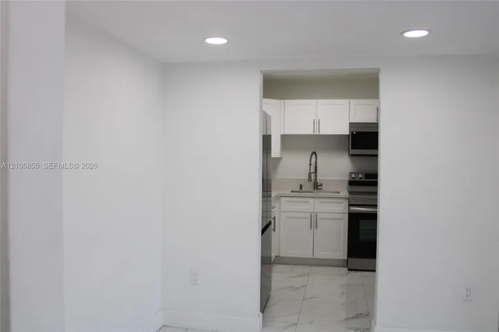 Kitchen featuring white shaker-style cabinetry, stainless steel appliances, a pull-down kitchen faucet, and stone-finish floor tiling with integrated recessed lighting