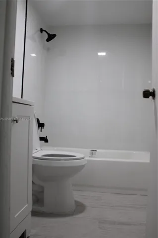 Full bathroom featuring a white bathtub, smooth wall panels, matte black shower head and hardware, and wood-finish flooring