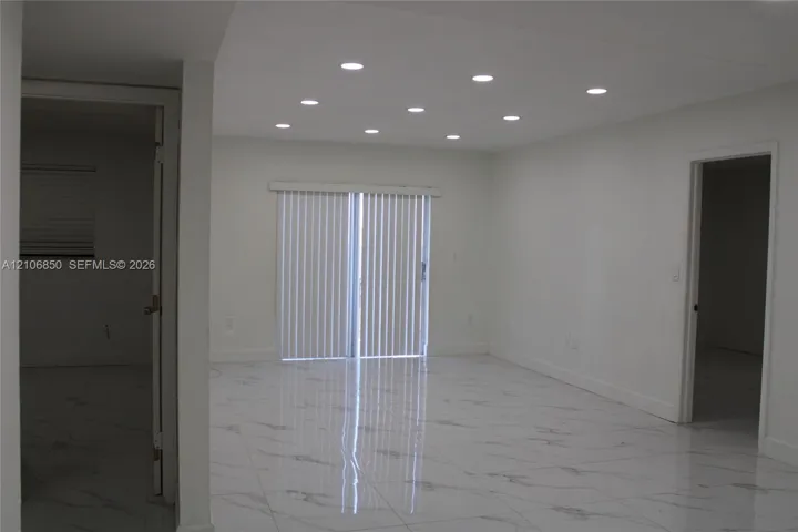 Interior space featuring large-format stone-finish tile flooring, recessed ceiling lighting, and sliding glass doors with vertical blinds