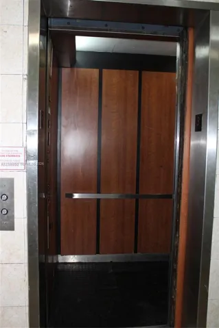 Elevator featuring wood-finish wall panels, stainless steel trim, and a horizontal metal handrail