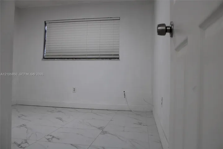 Room featuring white tile flooring with grey veining, neutral wall tones, and a window fitted with horizontal blinds