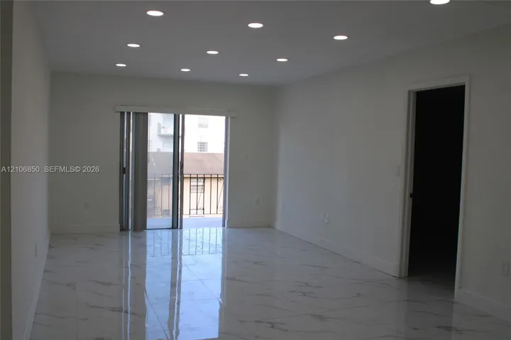 Interior space featuring high-gloss tile flooring with veining detail, recessed ceiling lighting, and sliding glass door access to an exterior balcony