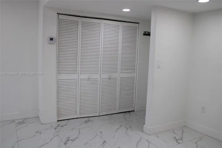 White louvered folding closet doors featuring circular hardware, complemented by large-format white tile flooring with grey veining and recessed ceiling lighting
