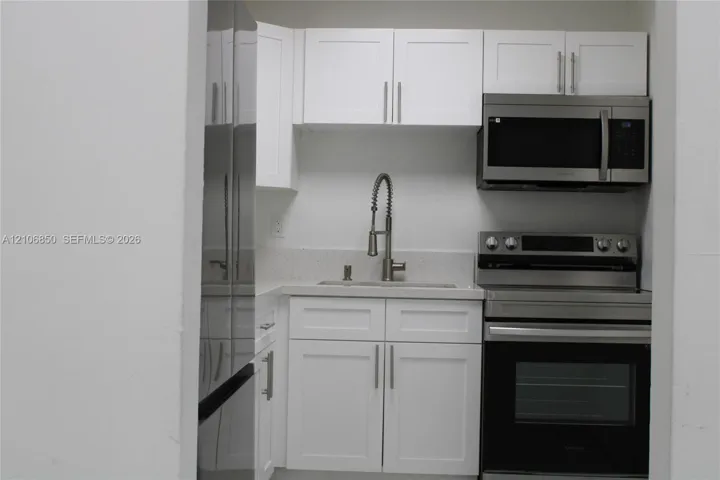Kitchenette featuring white Shaker-style cabinetry, stainless steel appliances, a stone-composite countertop, and a gooseneck faucet
