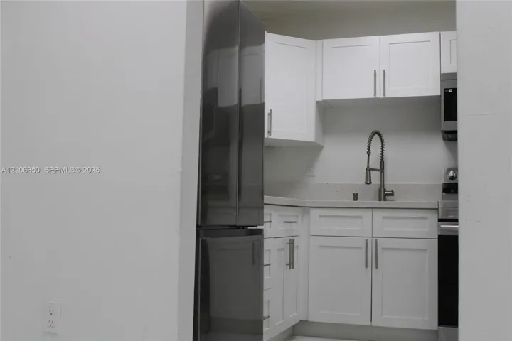 Kitchen featuring white shaker-style cabinetry, stainless steel refrigerator, stone-composite countertop, undermount sink with gooseneck faucet, and stainless steel microwave