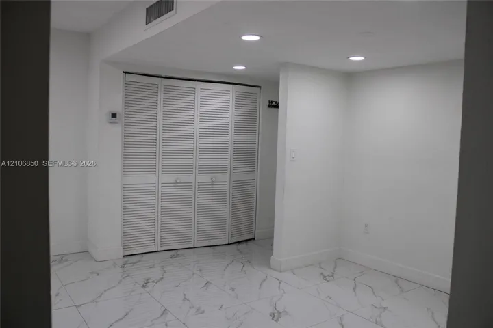 Interior space featuring white stone-finish flooring with grey veining, four-panel louvered closet doors, and recessed ceiling lighting
