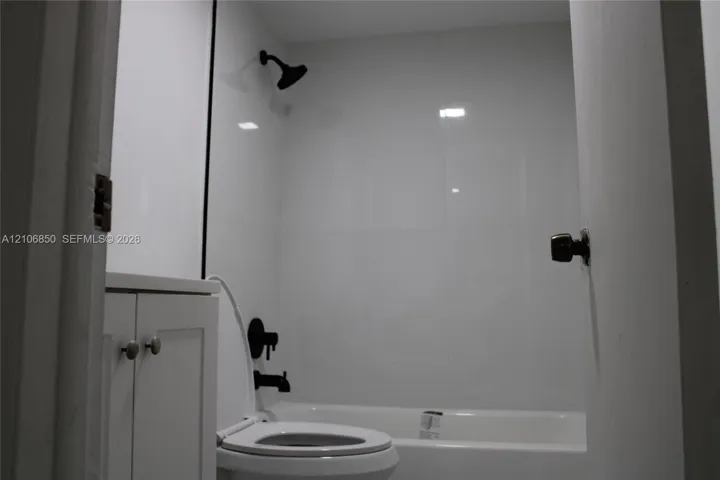 Bathroom featuring white panel shower surround, matte black showerhead and tub faucet, white vanity cabinet with circular pulls, and white standard toilet