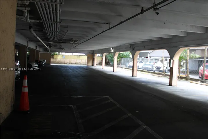 Covered parking area featuring concrete pillars, arched openings, and a paved surface