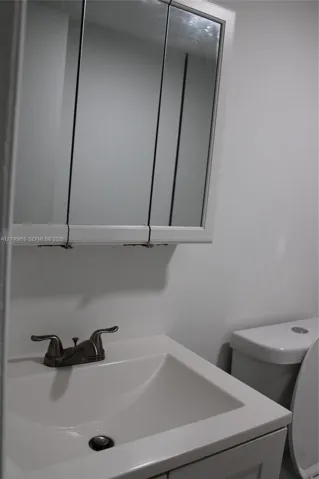 Tri-fold mirrored medicine cabinet, solid-surface vanity countertop with integrated basin, and dual-handle metallic faucet