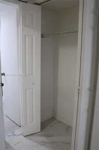 Storage closet featuring bi-fold panel doors and a built-in wire shelf, complemented by large-format stone-patterned tile flooring