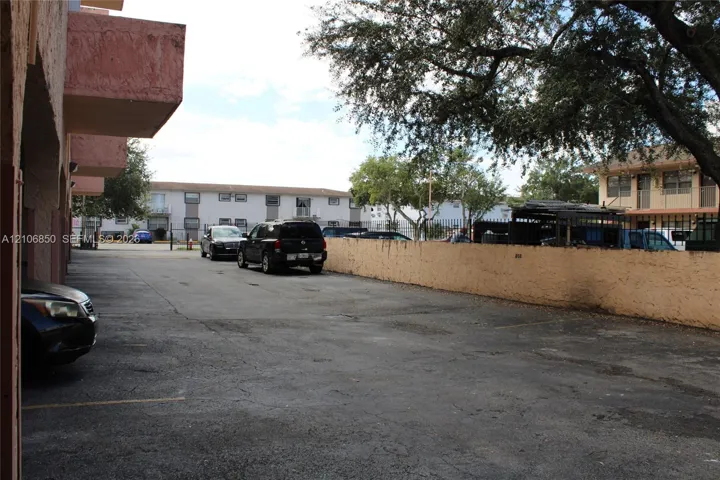 Asphalt-paved off-street parking area enclosed by a masonry perimeter wall and mature tree canopy
