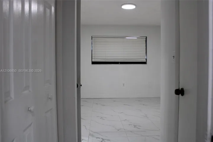 Interior room featuring large-format light-toned tile flooring with veining, multi-panel closet doors, and a window with horizontal blinds